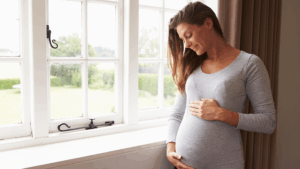 Mulher grávida sorrindo perto da janela, representando esperança e equilíbrio ao engravidar naturalmente após os 40.